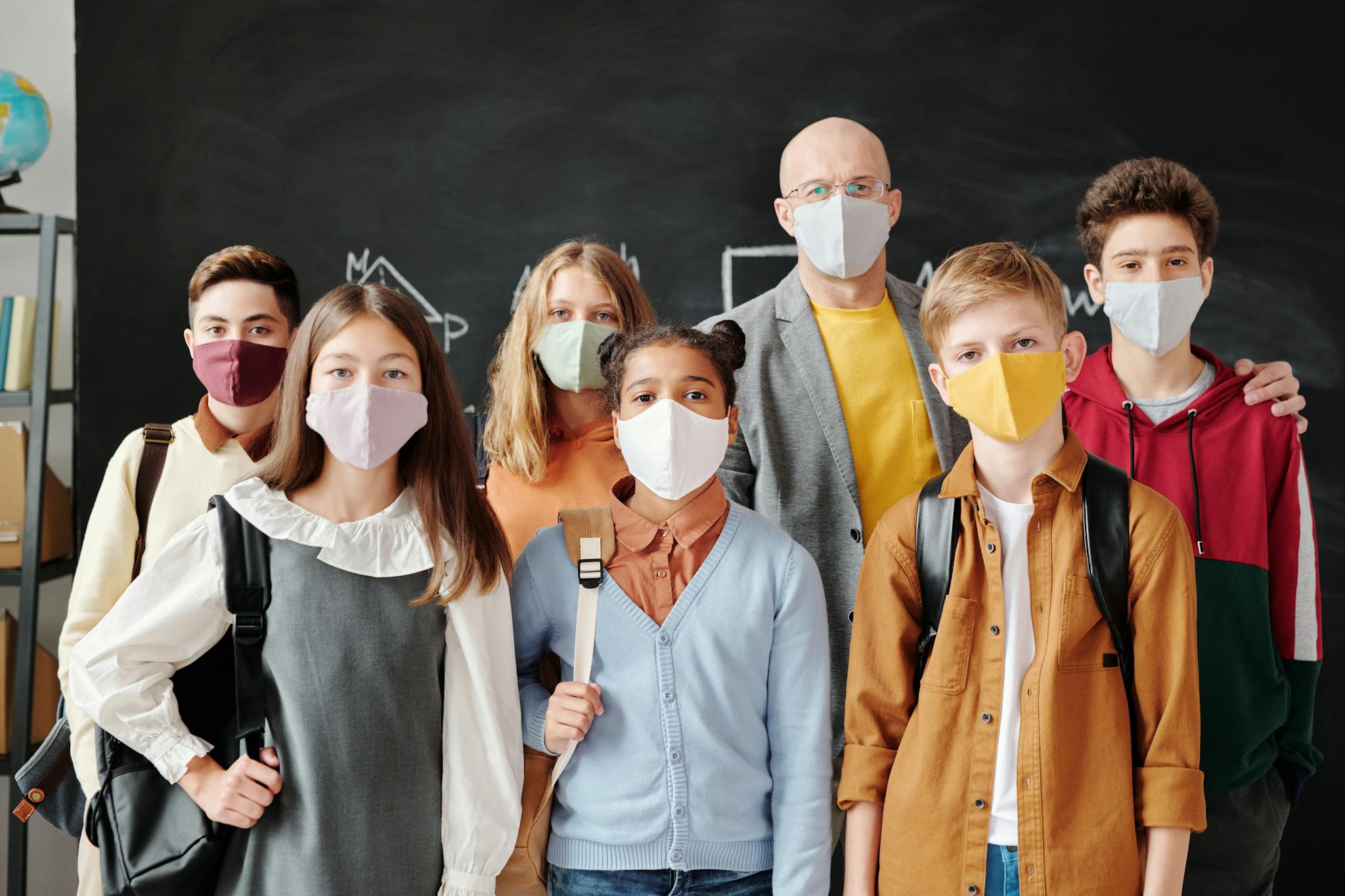 Group of students and a teacher in masks standing in a classroom during COVID-19 pandemic.